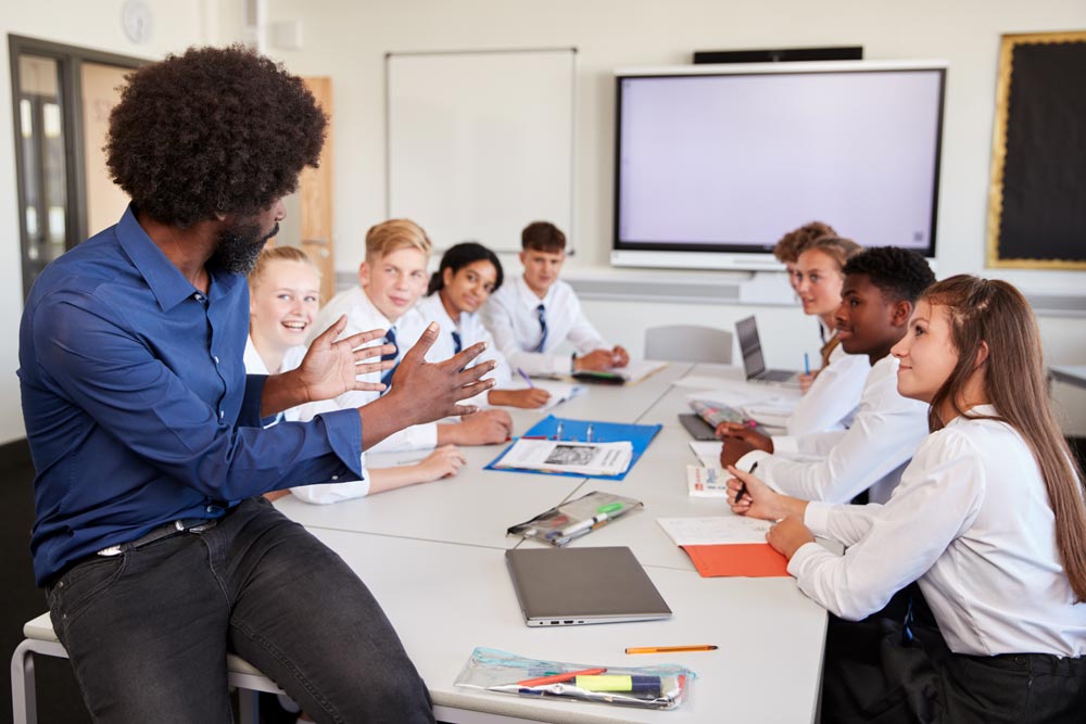 Male High School Teacher Sitting At Table With Teenage Pupils